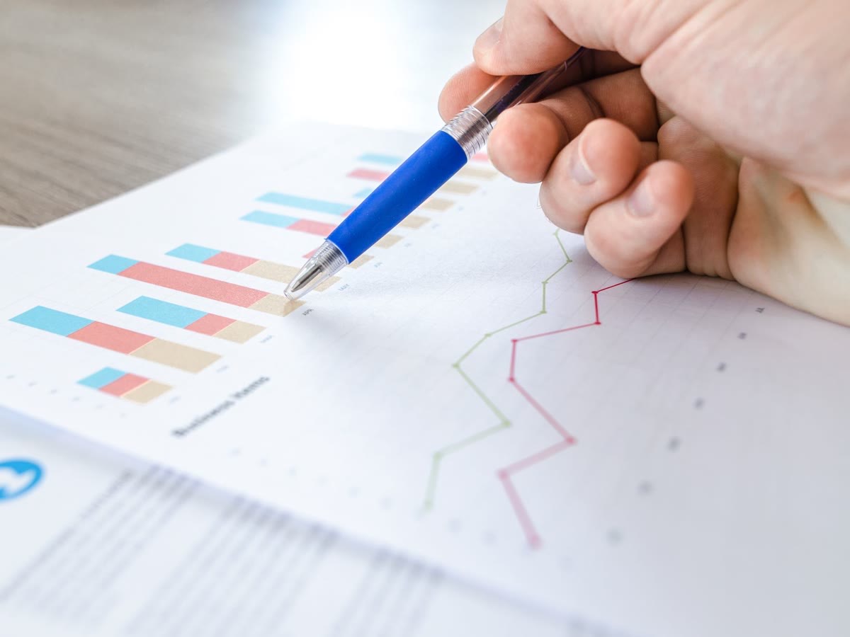 Mão analisando indicadores e gráficos em um documento sobre a mesa de trabalho