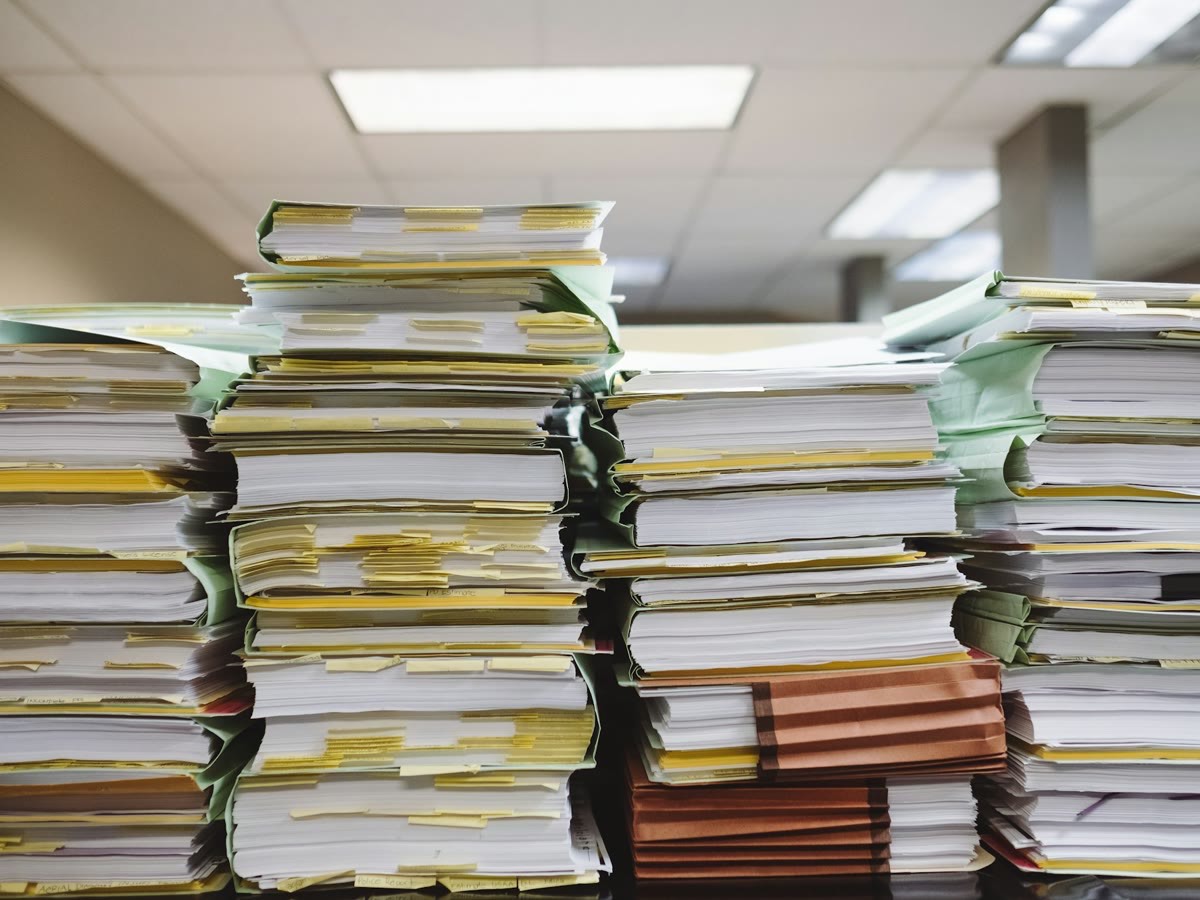 Pilhas desalinhadas de pastas e documentos empilhados sobre uma mesa de escritório