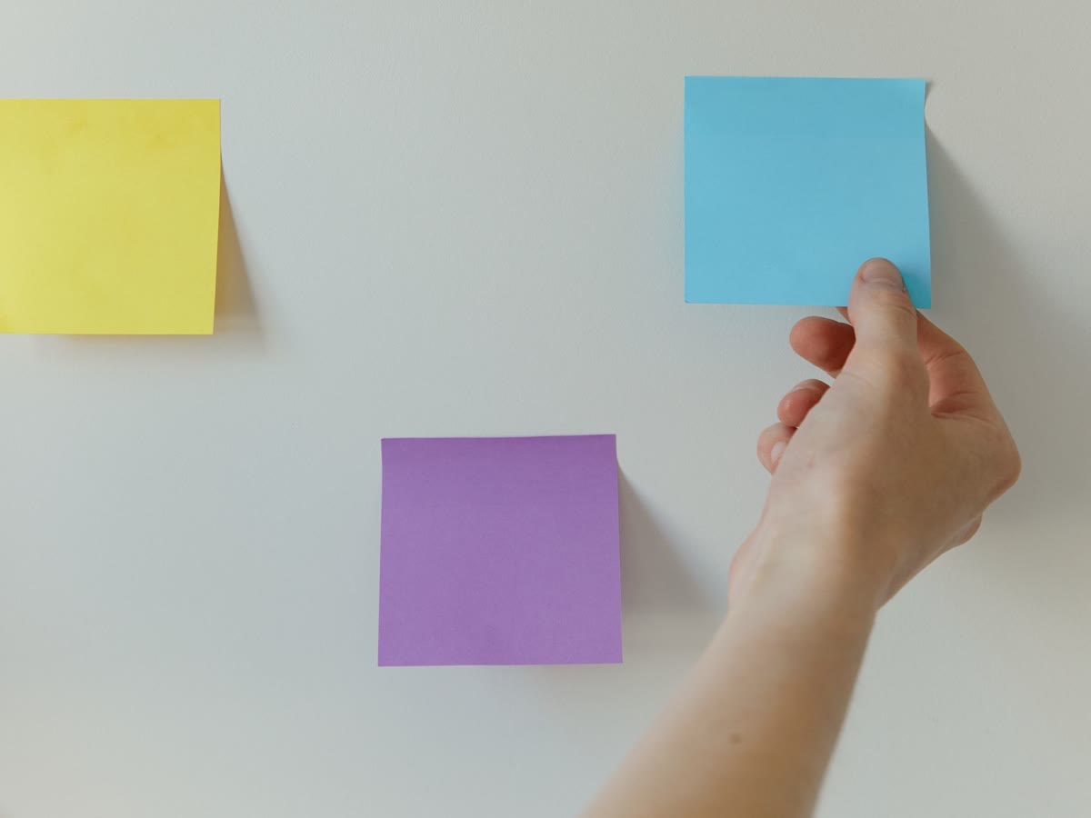Mão organizando notas adesivas coloridas nas colunas de um quadro de trabalho