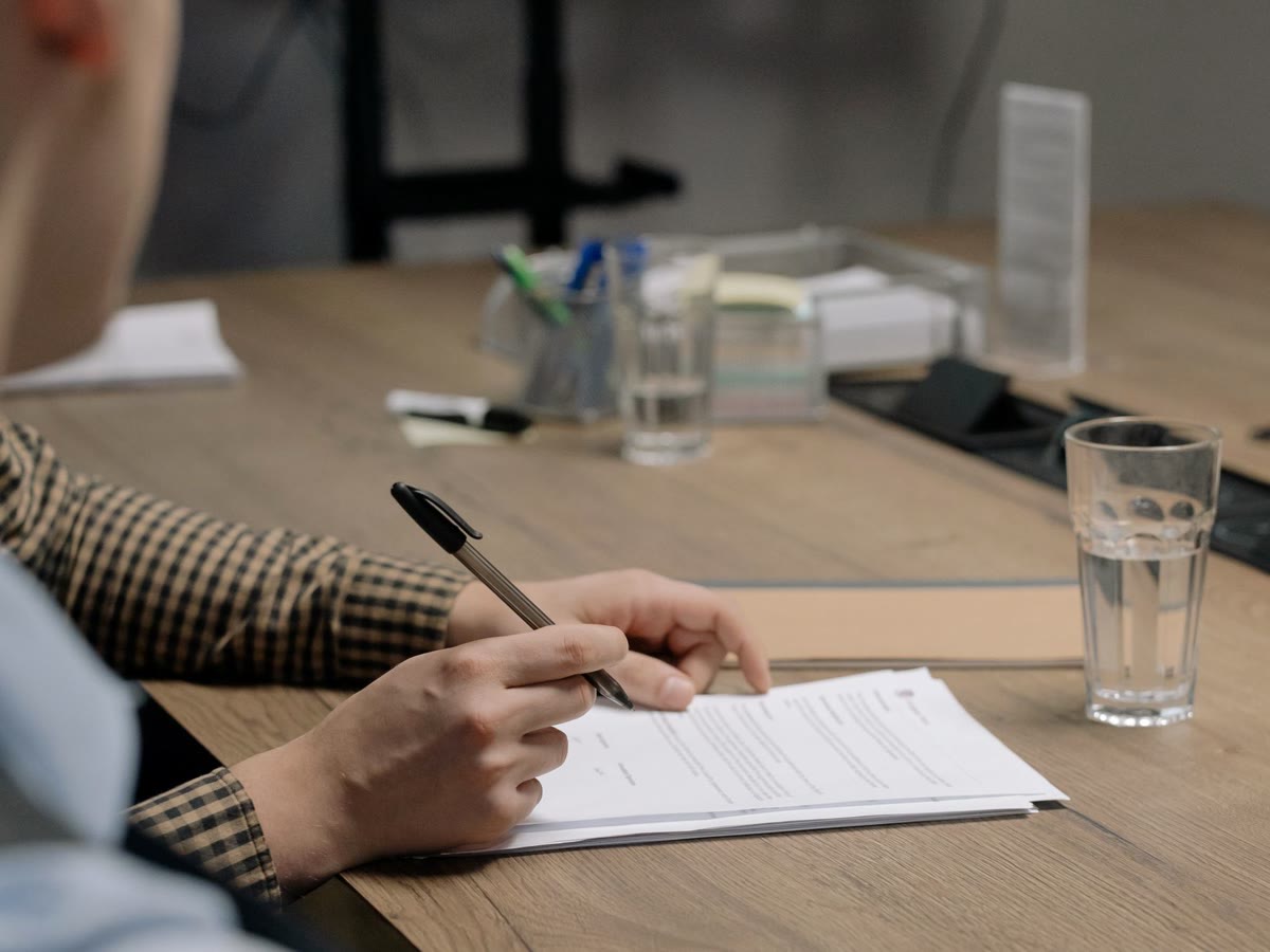 Mãos preenchendo documentos sobre a mesa de uma reunião de trabalho