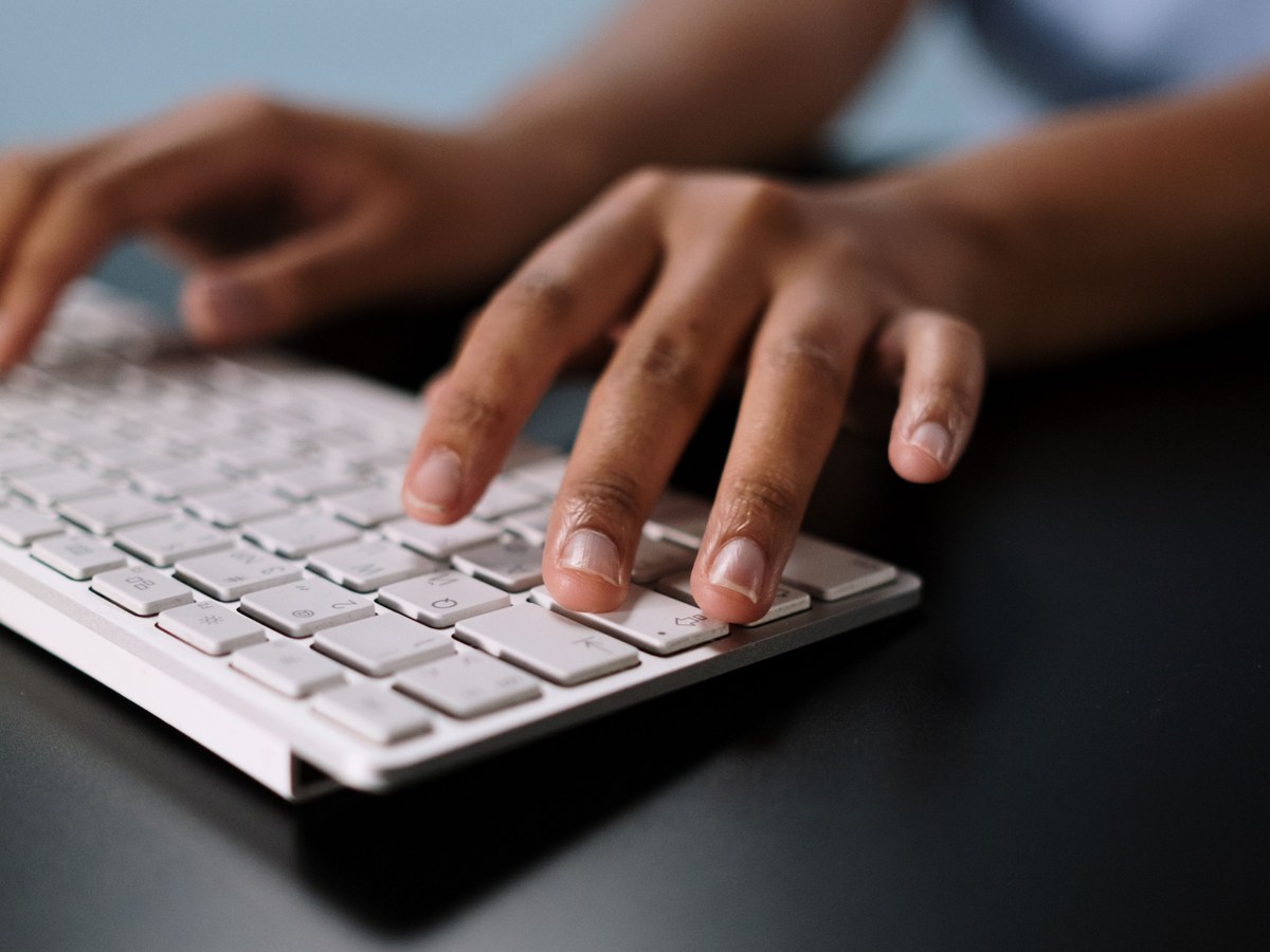 Mãos digitando em um teclado branco sobre uma mesa escura